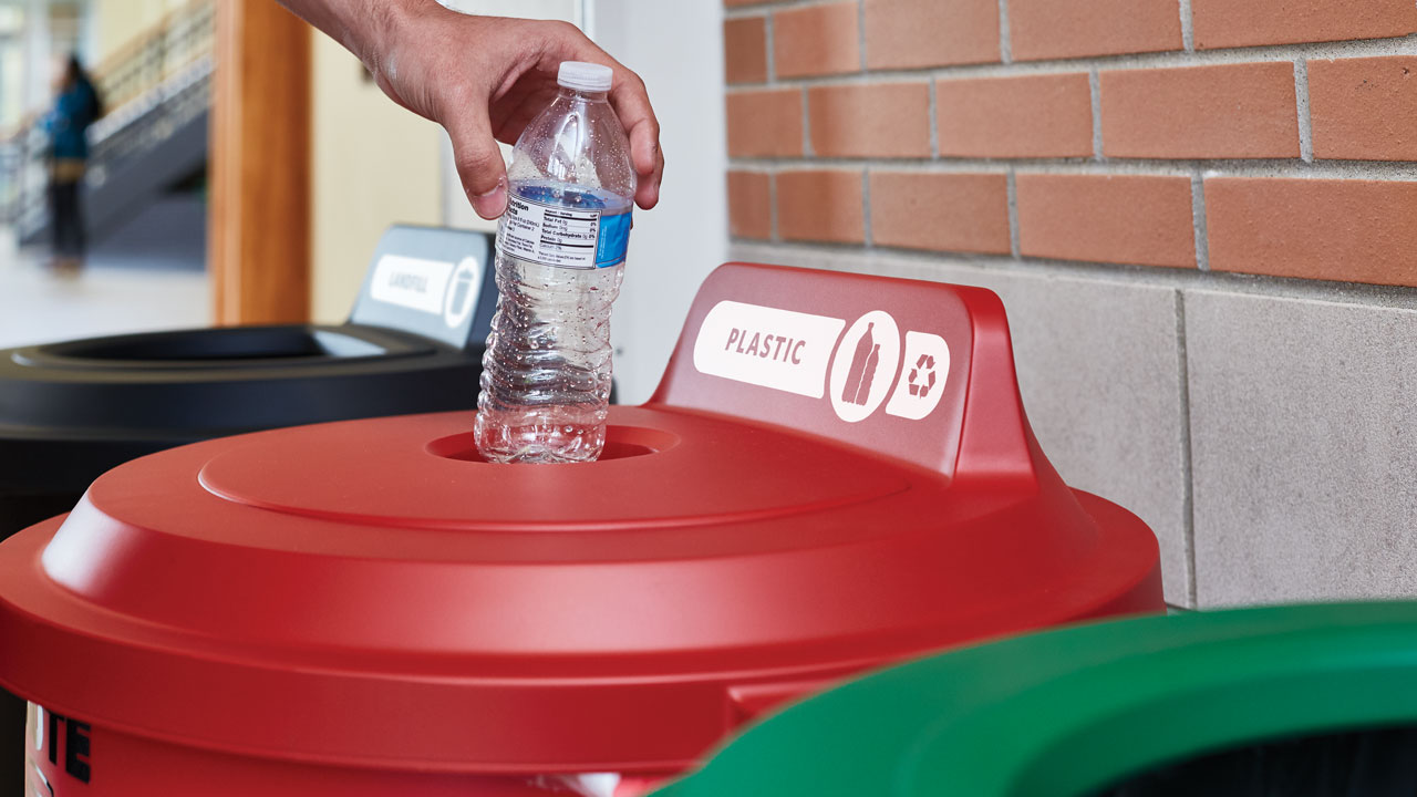 A person throwing a plastic water bottle on BRUTE® Vented Waste Container