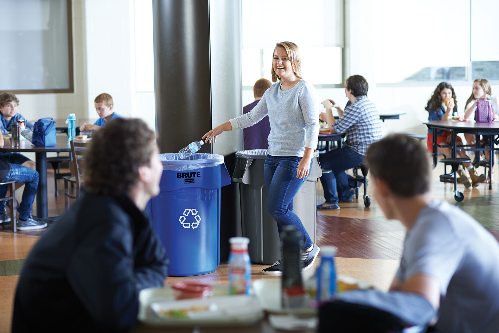 Woman throwing a plastic bottle on a Rubbermaid® BRUTE 32 Gallon Blue Round Recycling Can