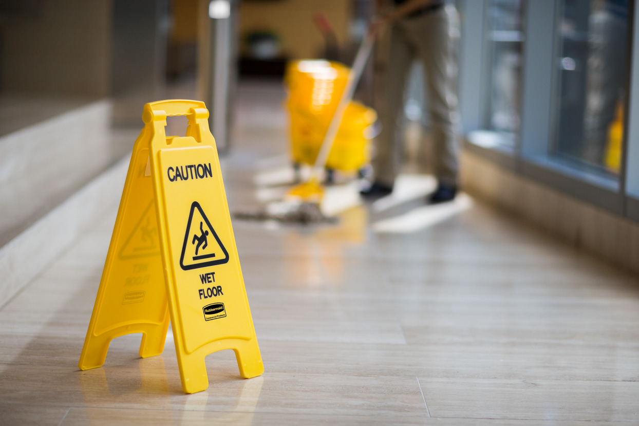 Wet floor caution sign next to a mop, informing people of a wet surface.